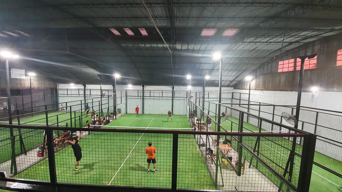 El galpón de Paddock de noche con las canchas de césped iluminadas y gente jugando